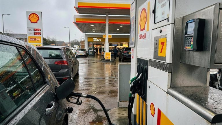 Contactless bank card being used at a Shell fuel pump on a wet UK forecourt, illustrating cashback on fuel